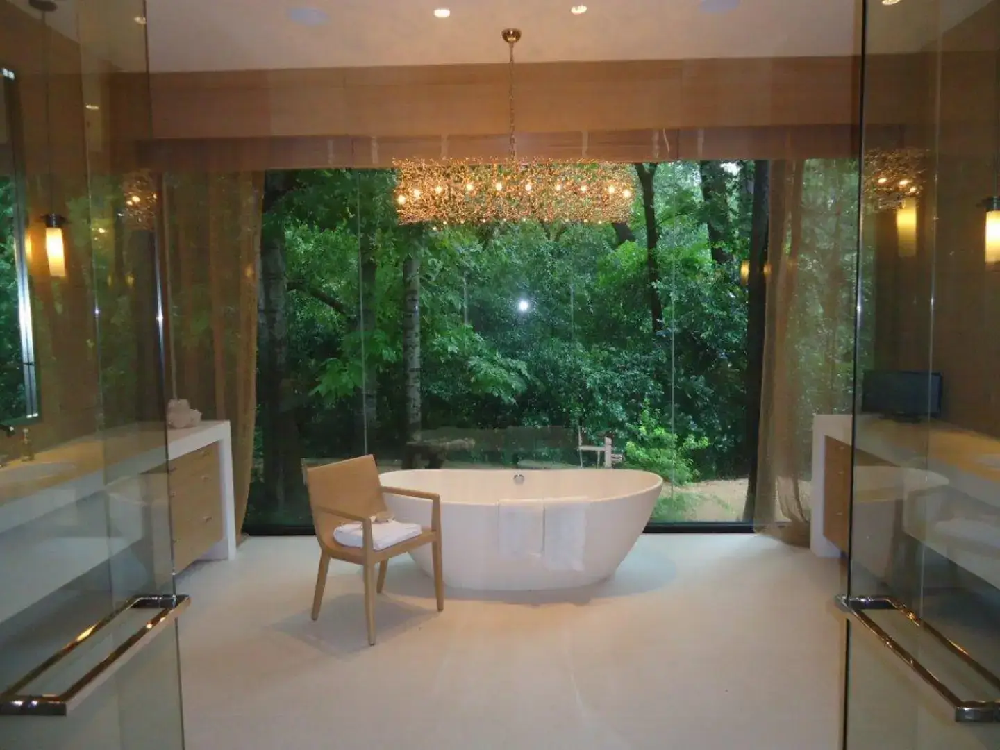 Bathroom with centered tub and floor-to-ceiling windows with drapery and wooden blinds.