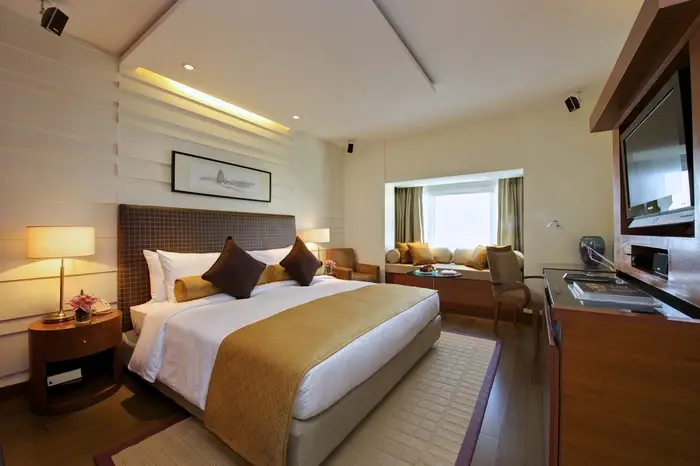 Modern hotel suite with king size bed, lamp, and window with drapery.
